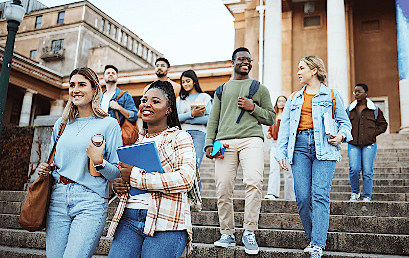 A group of college students are walking down the steps outside of a building.