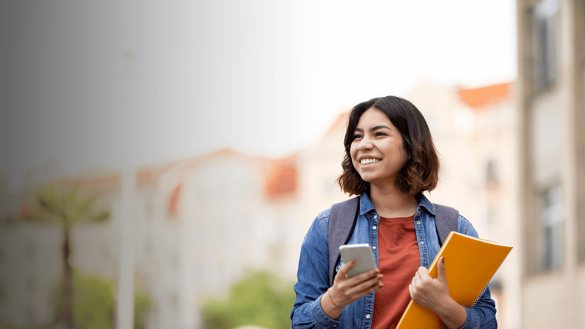 A young woman is on her phone, walking, with books.